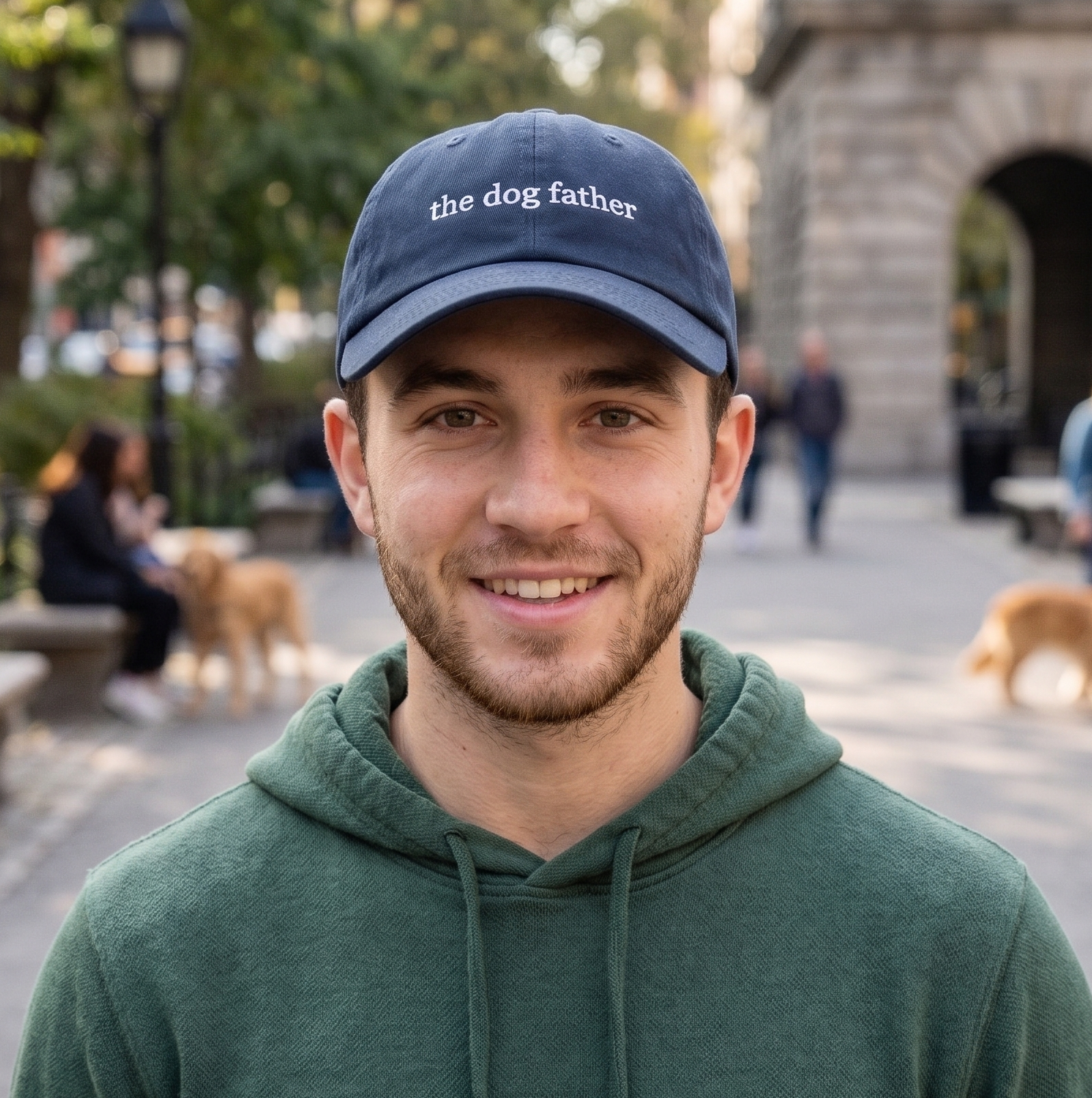Man wearing a cap with 'the dog father' text in an outdoor setting with people and dogs.